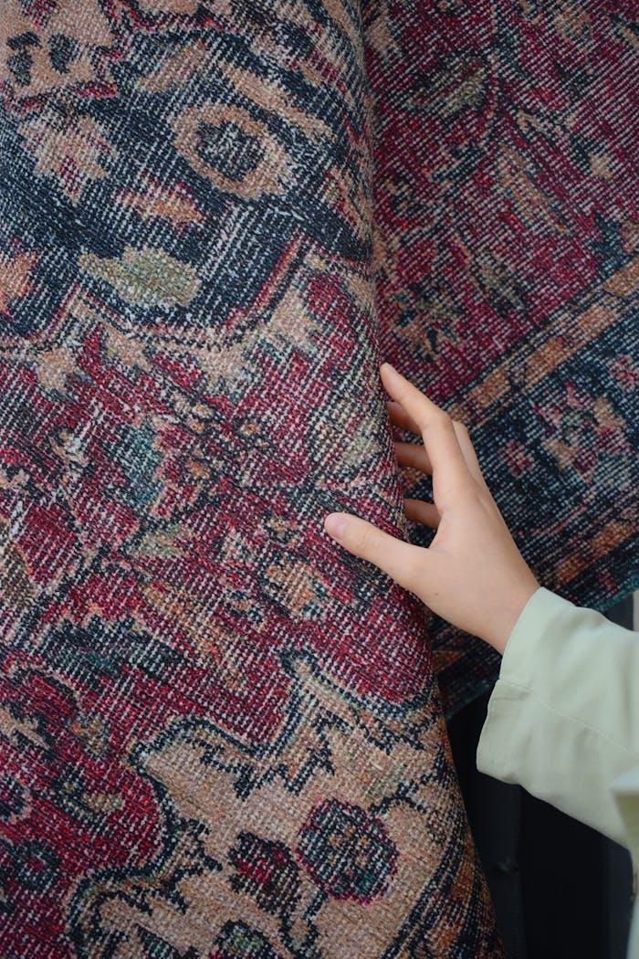 services-02 Close-up of a woman's hand touching a colorful, ornate handmade carpet with traditional textile design.