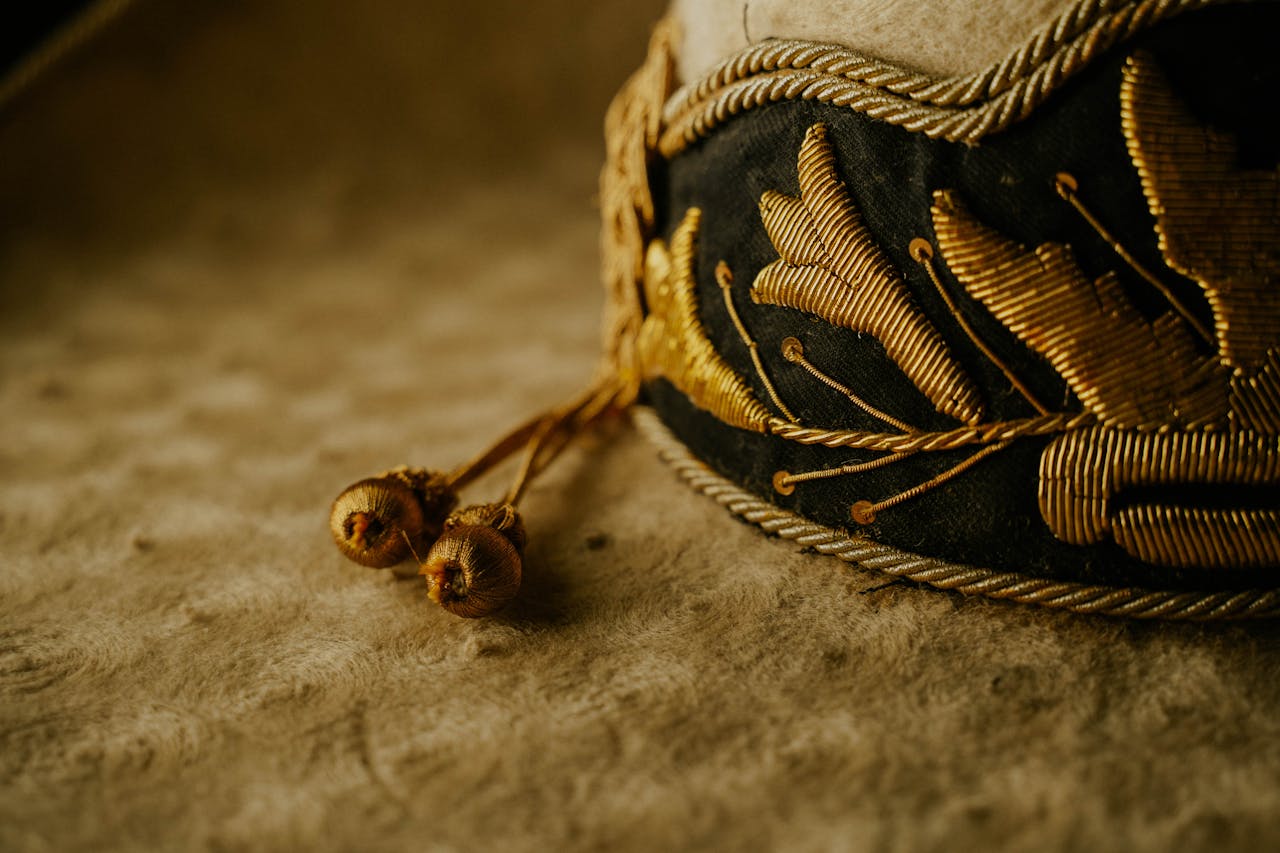 Close-up of a stylish embroidered hat with golden details and tassels on woolen fabric.