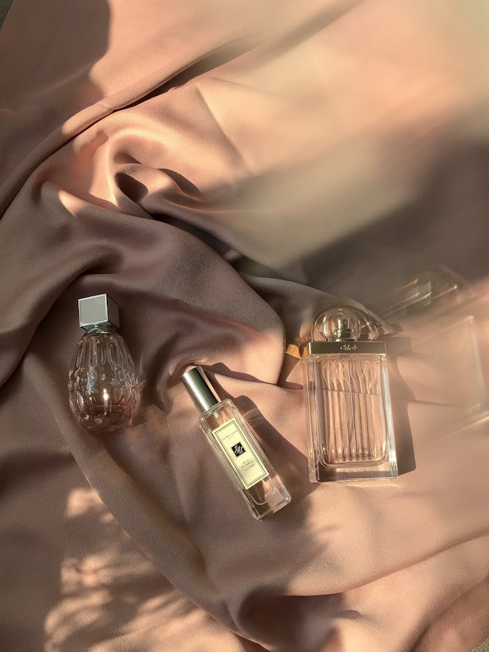 Aesthetic still life of elegant perfume bottles on luxurious pink satin, beautifully lit.