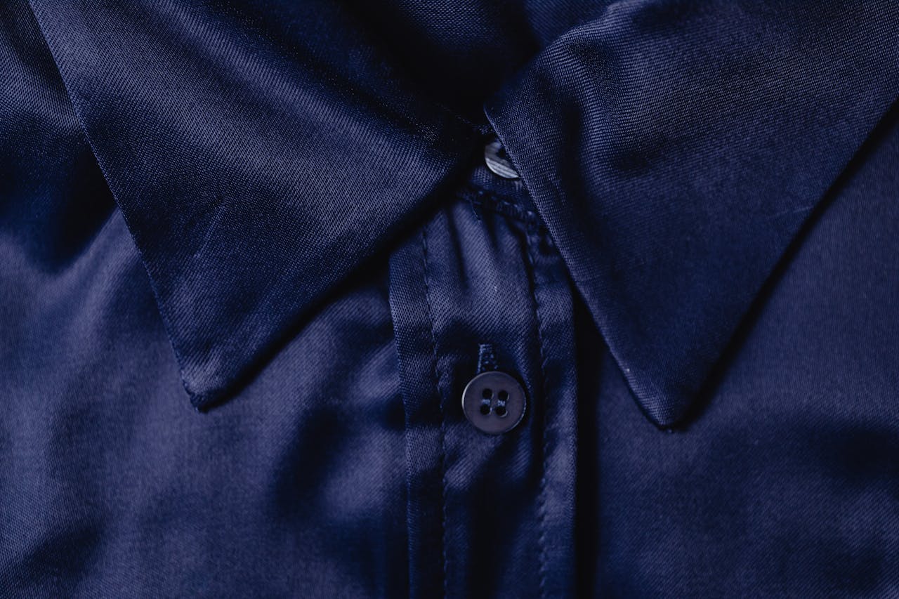Detailed close-up of a blue silk shirt collar highlighting fabric texture and button.