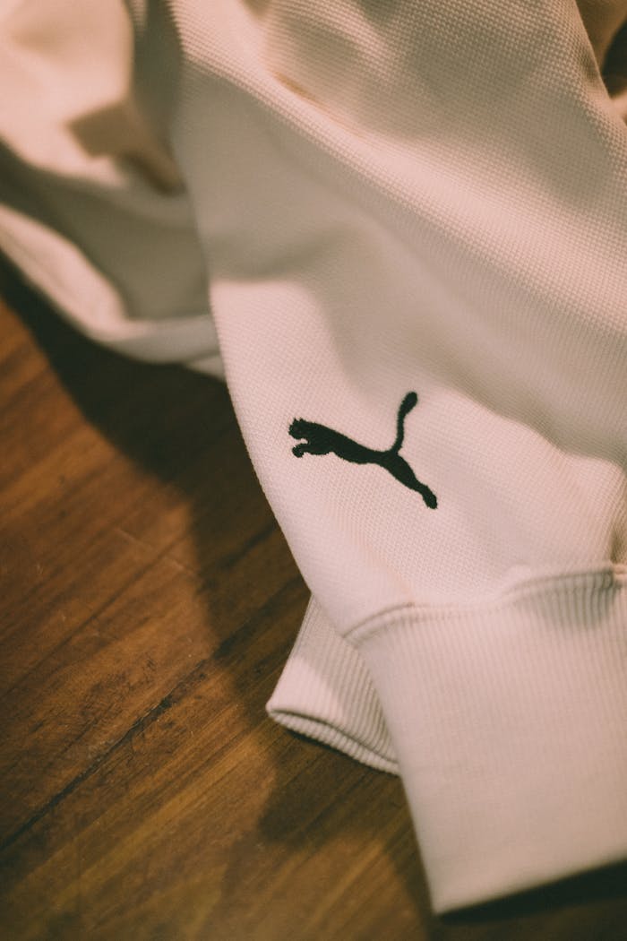 Artistic close-up of a white sweater featuring a black logo on wood background.