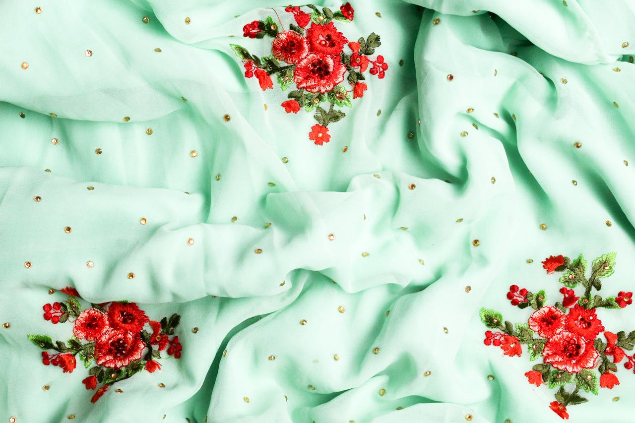 services-04 Luxurious green fabric adorned with intricate red flower embroidery, perfect for fashion and interior design.